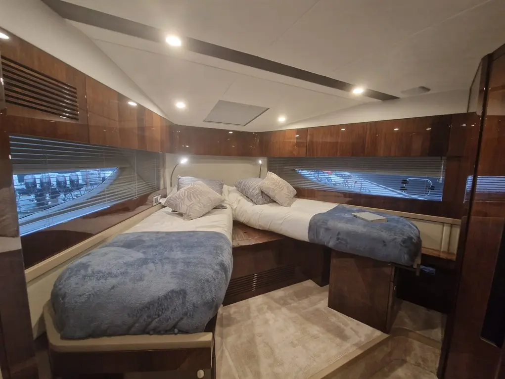 Luxury boat interior featuring two single beds with blue throws and decorative pillows, illuminated by warm LED lights.
